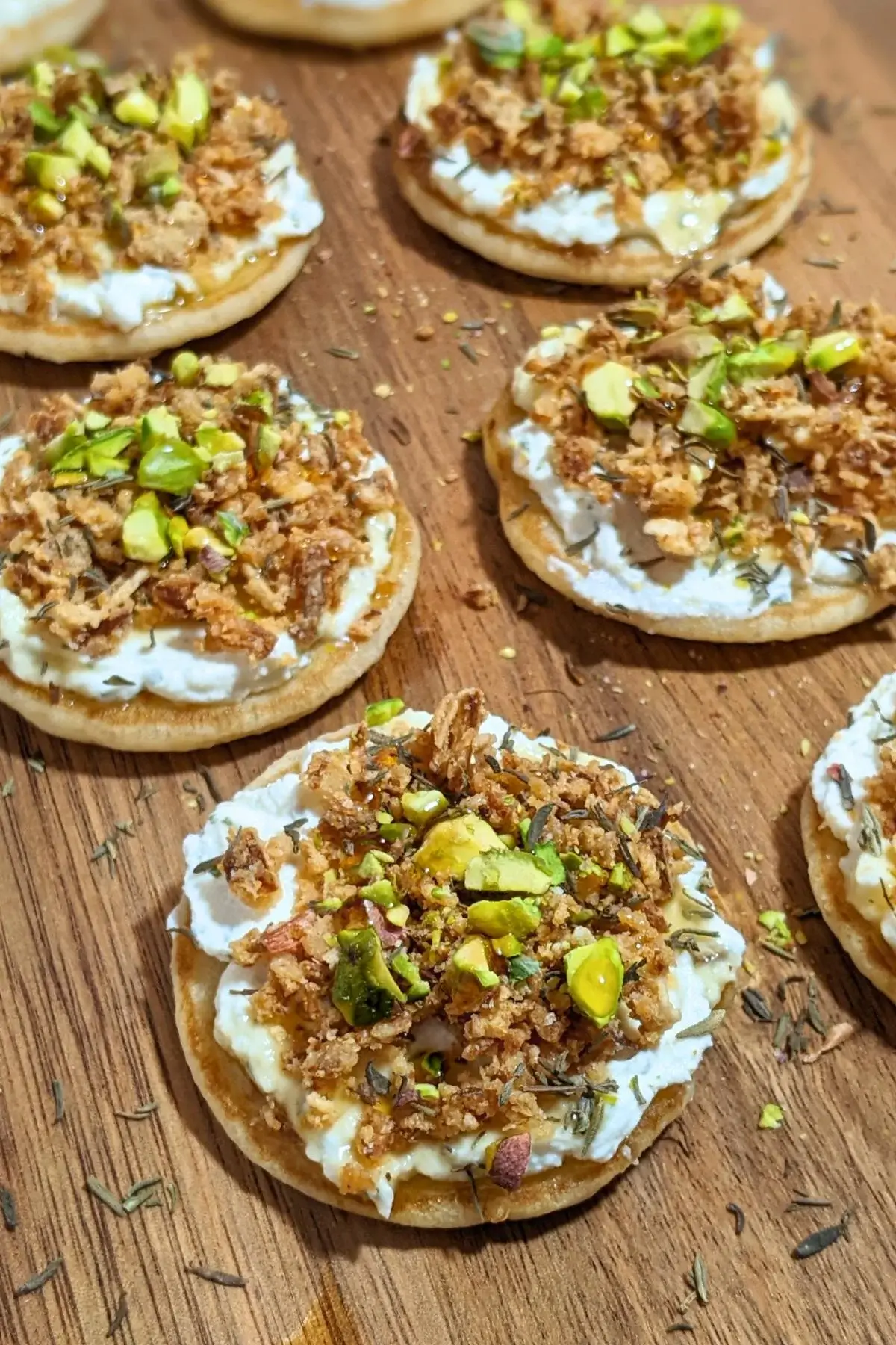 Mini Pancake Bites With Dried Onions - savory mini pancake canapes topped with a creamy herb-and-garlic cream cheese spread, crispy dried onions, maple syrup, and crushed pistachios for garnish.