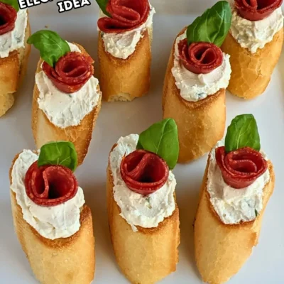 Pepperoni Rose Crostini Appetizers - oven-baked crostini toasts topped with homemade dried onion-fresh thyme cream cheese, slices of pepperoni rolled into roses, and fresh basil leaves for rose leaves.