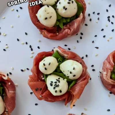 Prosciutto and Mini Mozzarella Bird Nests - easy 4-ingredient prosciutto and mozzarella appetizer with the prosciutto slices forming bird nests and the mini mozzarella balls sitting on green salad leaves as eggs, topped with black and white sesame seeds for speckles.