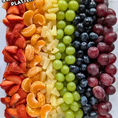 Rainbow Fruit Tray - colorful fruit platter in rainbow colors made with fruits and berries like strawberries, mandarin segments, canned pineapple pieces, green grapes, blue grapes, and dark red grapes.