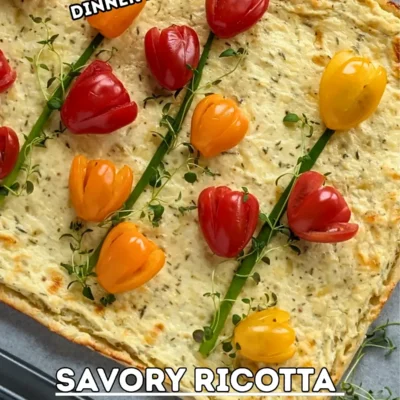 Savory Ricotta Puff Pastry Tart With Cherry Tomato Flowers - spring-themed puff pastry appetizer or dinner tart topped with a garlicky ricotta and grated Pecorino and cheese filling, topped with fresh red, orange, and yellow cherry tomatoes cut into shapes of tulips with green onions for stems and fresh thyme sprigs for leaves.